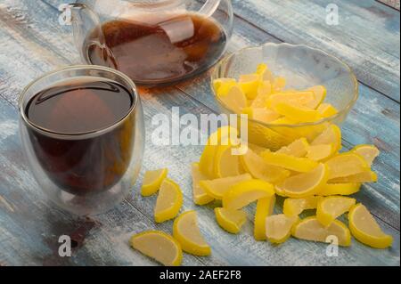 La marmellata di arance fette di limone, un bicchiere di tè nero e una teiera con infuso di tè su un sfondo di legno. Dolce con. Close up Foto Stock