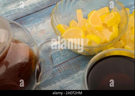 La marmellata di arance fette di limone, un bicchiere di tè nero e una teiera con infuso di tè su un sfondo di legno. Dolce con. Close up Foto Stock