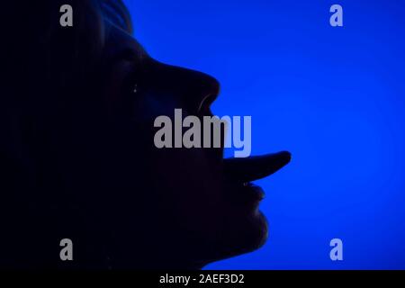Volto di donna che mostra la linguetta silhouette di fronte a sfondo blu Foto Stock