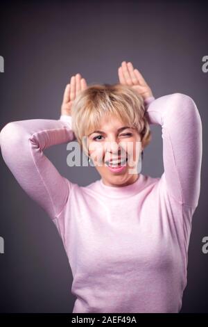 Donna con corti capelli biondi che mostra le orecchie gesto. Le persone e le emozioni concetto Foto Stock