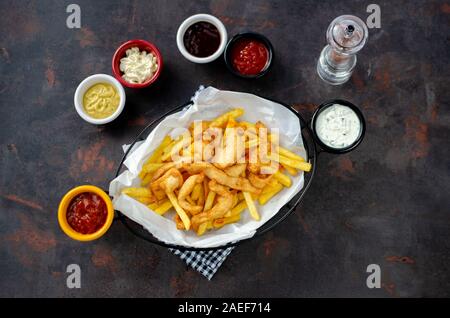 Cesto di patatine fritte e pollo con salse su sfondo scuro. Vista superiore Foto Stock
