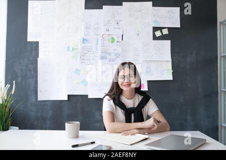 I giovani di successo economista femmina seduto da scrivania sullo sfondo di Blackboard Foto Stock