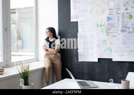 Giovani stanchi imprenditrice in informale guardando attraverso la finestrella in office Foto Stock