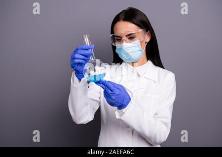 Ritratto di uno scienziato concentrato il lavoro della donna in lab rendere nuovo vaccino analisi chimico liquido blu tenere pallone Usura mantello bianco maschera occhiali guanti Foto Stock