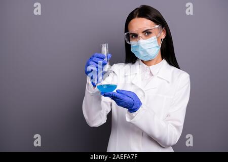 Ritratto di scienziato di successo donna presente il suo nuovo farmaco contro il cancro ha tenere nel suo pallone liquido blu indossare i guanti di sicurezza occhiali white Foto Stock