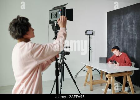 Giovane uomo informale nel preparare la telecamera video prima di effettuare le riprese in studio Foto Stock