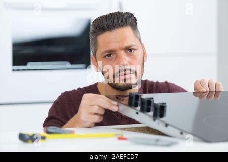 Giovani repairman installazione fornello ad induzione in cucina Foto Stock