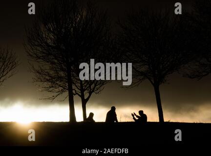 Hannover, Germania. 09Dec, 2019. Le sagome di tre uomini si stagliano contro il Rising Sun e nuvole scure. Credito: Julian Stratenschulte/dpa/Alamy Live News Foto Stock