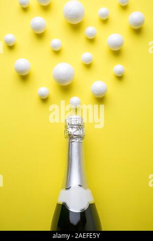 Piatto di laici bottiglia di champagne e bolle costituito da polistirolo palle contro sfondo giallo minimo drink creativi concetto. Foto Stock