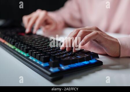 Mani di adolescente sopra i tasti della tastiera del computer digitando mentre è seduto da scrivania Foto Stock