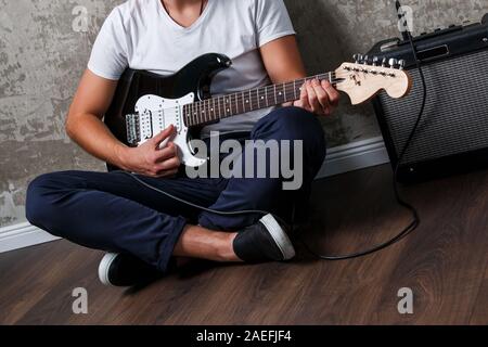 Elegante ragazzo con una chitarra seduto sul pavimento Foto Stock