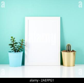 Vuoto telaio bianco, impianti cactus su un tavolo bianco contro la parete di blu. Mockup con copia spazio. Foto Stock