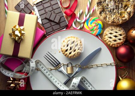 Posate su una piastra con lucchetto circondato con cibo di natale e decorazioni Foto Stock