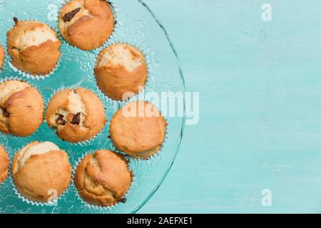 Deliziosa casa muffin alla vaniglia con cioccolato sulla lastra di vetro su sfondo turchese. Dessert per la celebrazione, festa o uno spuntino. Tortine. Foto Stock