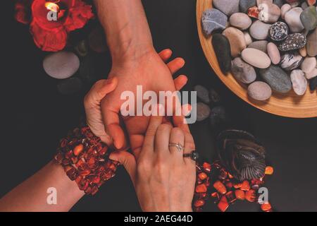 Giovani fortune teller divini la mano del giovane uomo intorno a candele e altri paraphernalia magico. La divina magia e occultismo concetto. La Divinazione. Parte superiore Foto Stock