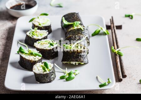 Vegano rotoli di sushi con avocado, cetriolo, tofu e piantine su sfondo grigio. Sano cibo vegan concetto. Foto Stock