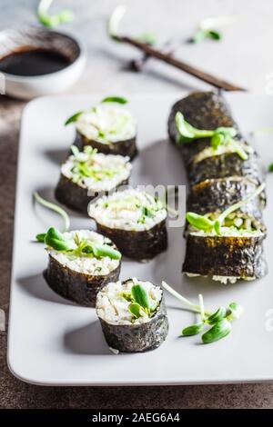 Vegano rotoli di sushi con avocado, cetriolo, tofu e piantine su sfondo grigio. Sano cibo vegan concetto. Foto Stock