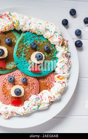 Multi-colore di pancake con frutta e panna montata per bambini su una piastra bianca, sfondo bianco. Foto Stock
