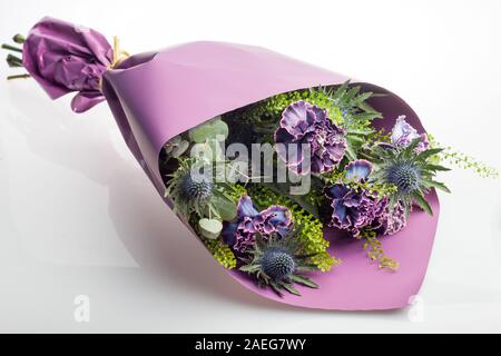 Composizione floreale di fiori di garofani, foglie di thistle ed eucalipto. Bouquet di fiori di colore violaceo, violaceo e violaceo in carta viola Foto Stock