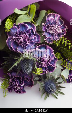 Composizione floreale di fiori di garofani, foglie di thistle ed eucalipto. Bouquet di fiori di colore violaceo, violaceo e violaceo in carta viola Foto Stock