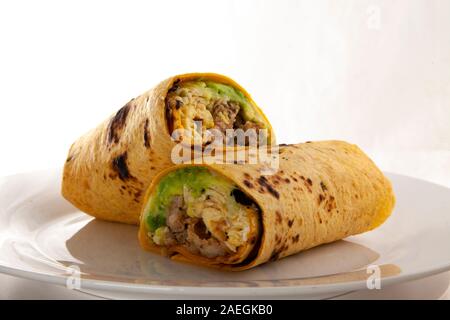 Una colazione burrito con uova, salsicce, formaggio, e avocado in una tortilla avvolgere su una piastra bianca di fronte a uno sfondo bianco. Foto Stock