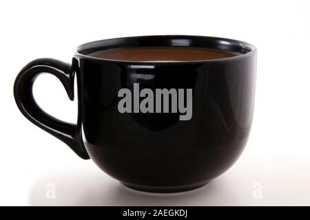 Il caffè con il latte o la crema di latte in una tazza nera davanti a uno sfondo bianco. Foto Stock