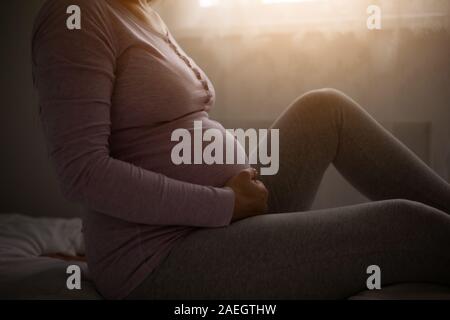 Donna incinta mentre tiene il suo stomaco e un momento di relax a casa. Foto Stock