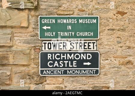 Via segni sulla parete della torre Street di Richmond per il Green Howards Museum, Chiesa della Santa Trinità e Richmond Castle. North Yorkshire, Inghilterra Foto Stock