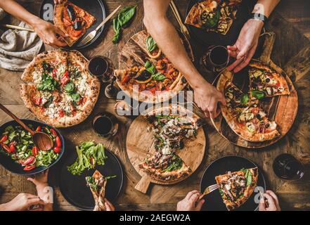 Persone mangiare diversi tipi di pizza, insalate e bere il vino Foto Stock