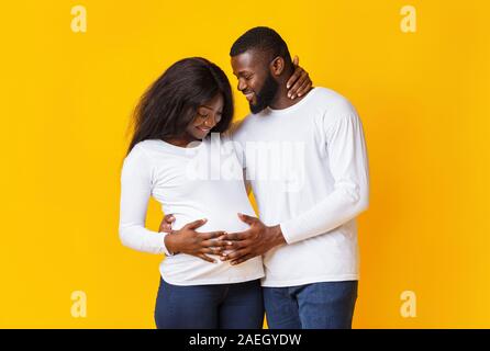 Incinta giovane in amore abbracciando e parlare su sfondo giallo Foto Stock