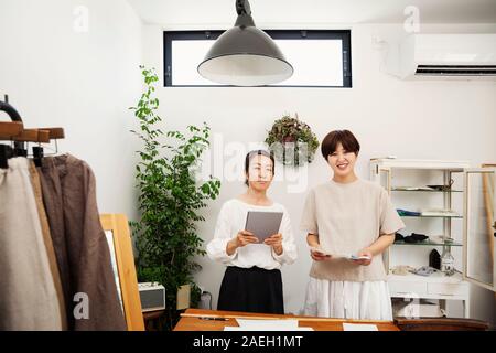 Due donne giapponesi in piedi in una piccola boutique di moda, tenendo digitale compressa, sorridente alla fotocamera. Foto Stock