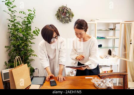 Due donne giapponesi in piedi in una piccola boutique di moda, guardando a tavoletta digitale. Foto Stock