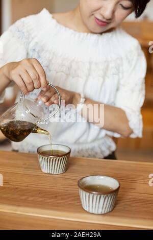 Donna Giapponese seduti ad un tavolo in un vegetariano cafe, versando il tè. Foto Stock
