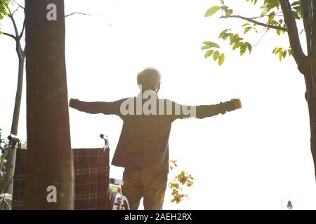 Vista posteriore di asian senior uomo in piedi dalla sedia a rotelle con le braccia aperte Foto Stock