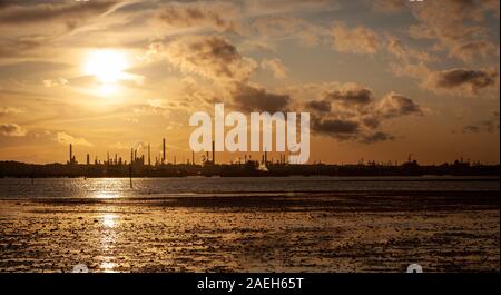 Vista panoramica del tramonto dietro stagliano raffineria di petrolio su acqua di Southampton con fango flats in primo piano Foto Stock