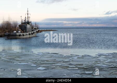 Il rimorchiatore è al molo del porto di Cronštadt. Il primo ghiaccio sull'acqua. San Pietroburgo è all'orizzonte. Foto Stock