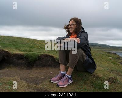 Donna seduta su di una collina, Downpatrick Head, Killala, County Mayo, Irlanda Foto Stock