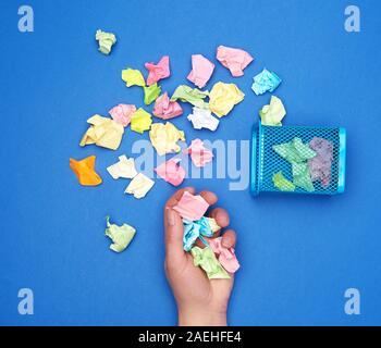 Mano femmina trattiene un mazzetto di accartocciata multi-colore di pezzi di carta, accanto a un metallo spazzatura, Foto Stock