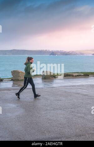 Una giovane donna jogging lungo un vuoto costiera del parco auto in Newquay in Cornovaglia. Foto Stock