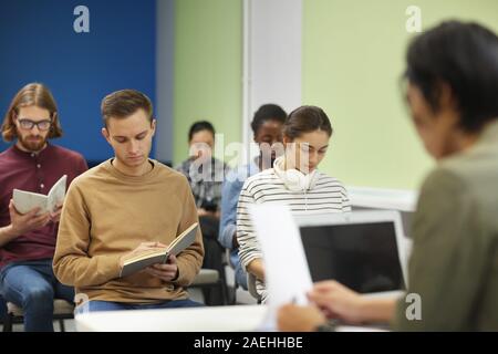 Gruppo multietnico di giovani persone sedute e la scrittura nei notebook mentre insegnante la lettura di una conferenza Foto Stock