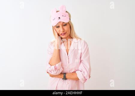 Medioevo donna che indossa la maschera del sonno e pigiama isolato su sfondo bianco pensare guardando stanco ed annoiato con depressione problemi con attraversata una Foto Stock