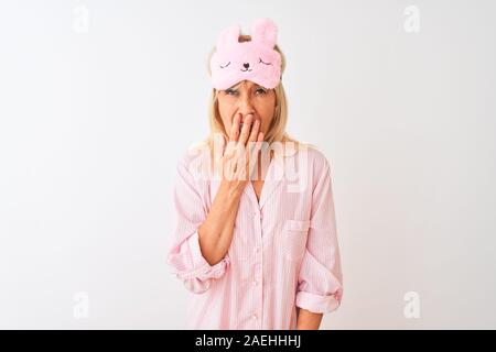 Medioevo donna che indossa la maschera del sonno e pigiama isolato su sfondo bianco annoiati sbadigli stanchi che copre la bocca con la mano. Inquieto e sonnolenza. Foto Stock