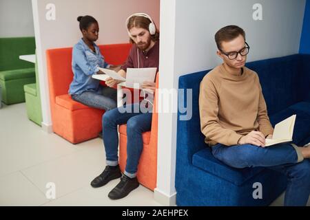 I giovani seduti su divani colorati e la lettura di libri e documenti in sala di attesa Foto Stock