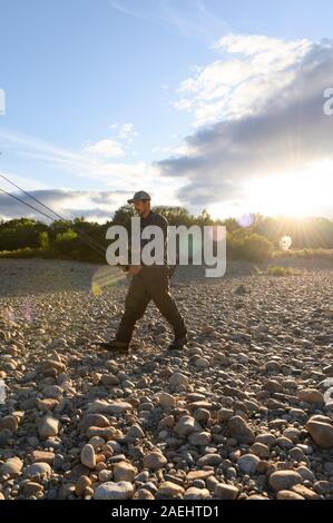 Un giovane uomo che cammina verso il fiume per andare la pesca con la mosca in una giornata di sole Foto Stock