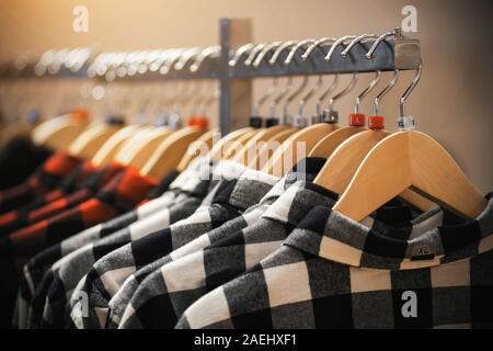 Nel negozio di abbigliamento, giovani alla moda plaid camicie in rosso e bianco, illuminata da luce, appendere su appendiabiti. Foto Stock