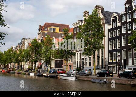 Vista del canal, parcheggiato barche, automobili, alberi e storici edifici tradizionali che mostra architettura olandese stile in Amsterdam. Si tratta di un giorno d'estate. Foto Stock