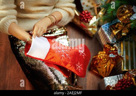 Primo piano sul giovane donna in oro zecchino gonna e maglione bianco sotto albero di Natale decorato vicino presente scatole avviene qualcosa al di fuori del rosso s di Natale Foto Stock