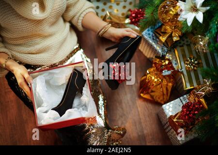 Elegante massaia in oro zecchino gonna e maglione bianco sotto albero di Natale decorato vicino presente azienda scatole regalo di Natale scatola nera e sho Foto Stock