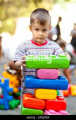 Carino ragazzo giocando con il giocattolo edili blocchi colorati. Il capretto con faccia felice giocando con mattoni di plastica. Plastica giocattolo di grandi dimensioni. Foto Stock