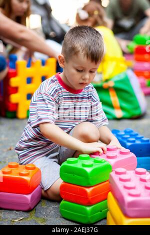 Carino ragazzo giocando con il giocattolo edili blocchi colorati. Il capretto con faccia felice giocando con mattoni di plastica. Plastica giocattolo di grandi dimensioni. Foto Stock